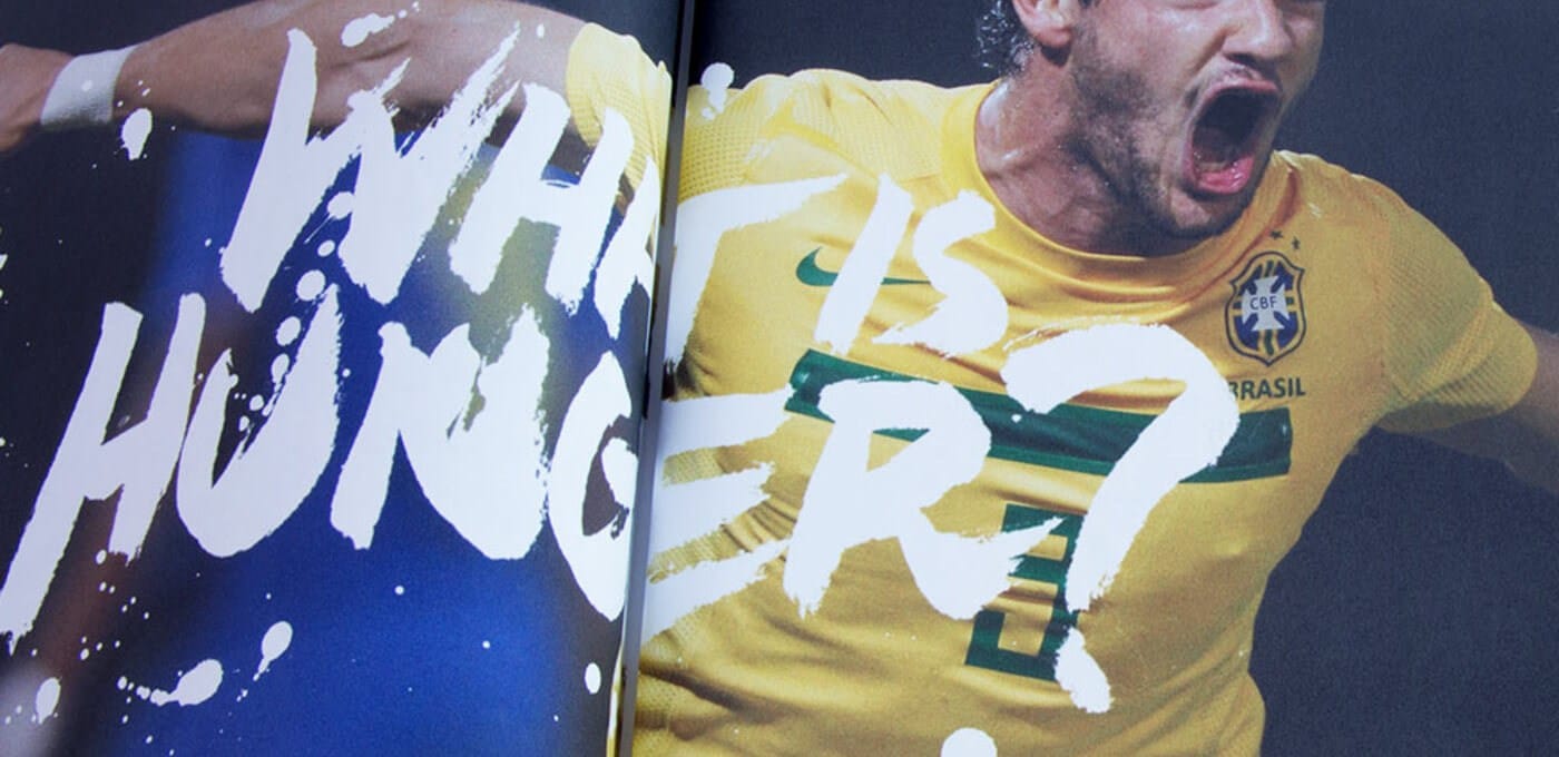 Two-page spread of a person in a yellow Brazil jersey celebrating with mouth open, overlaid by bold white brush-stroke text across the pages.