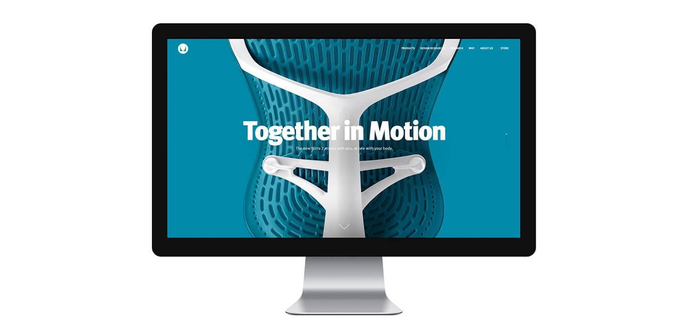 Desktop monitor displaying a blue background with a white ergonomic back-support graphic and the phrase "Together in Motion."