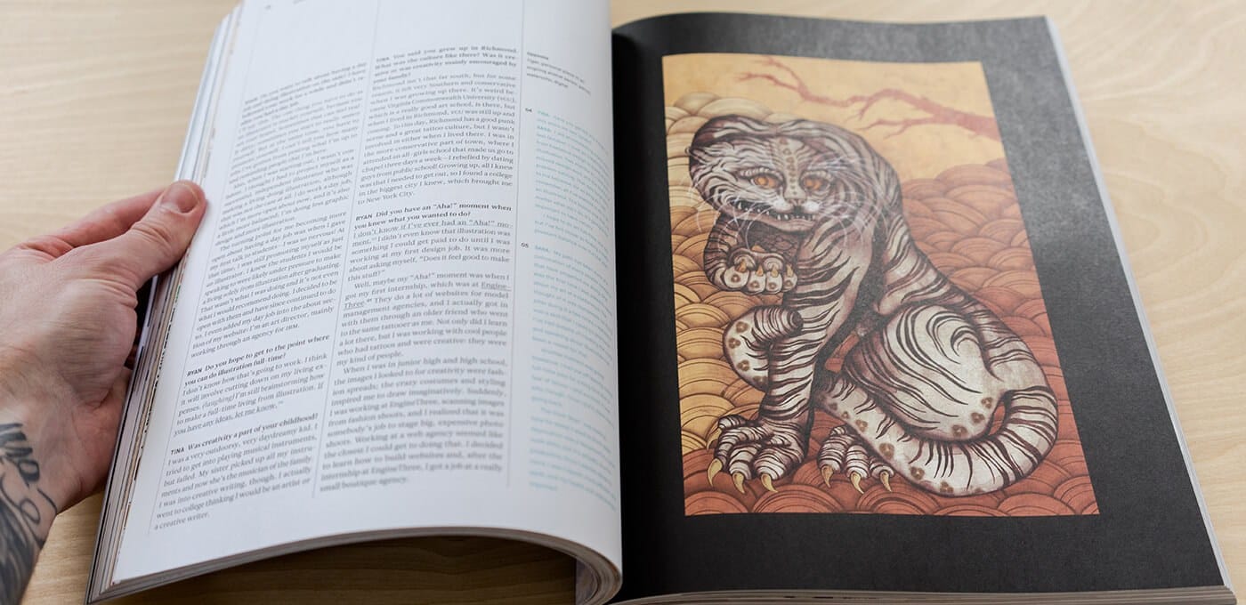 A hand holds open magazine; left page has dense column text, right page shows a framed orange-toned illustration of a tiger-like creature.