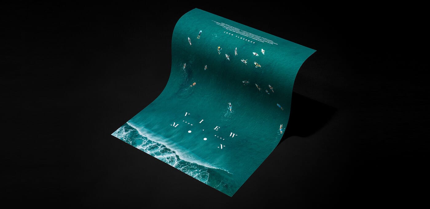 A curled teal poster floats against a black backdrop, showing an ocean scene with surfers and white text, with foamy waves at the bottom.