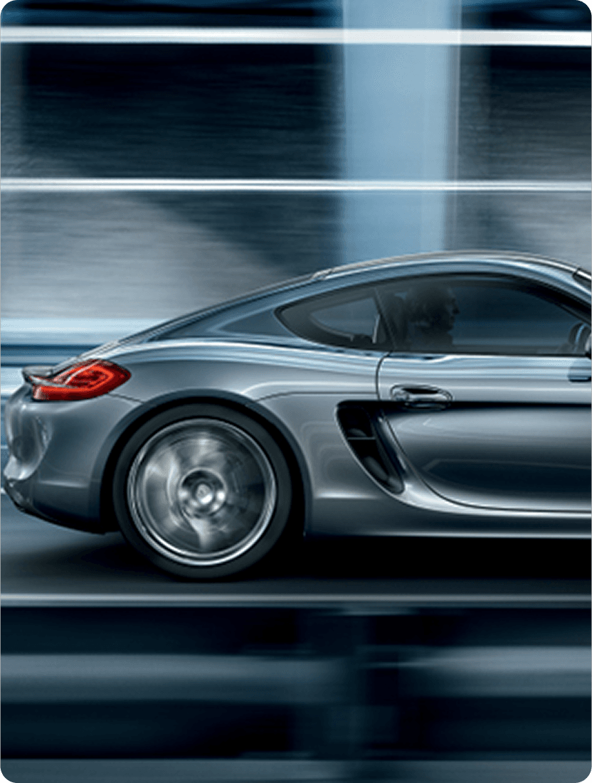 Side profile of a silver sports car speeding along a blurred road with a blue glass building in the background.