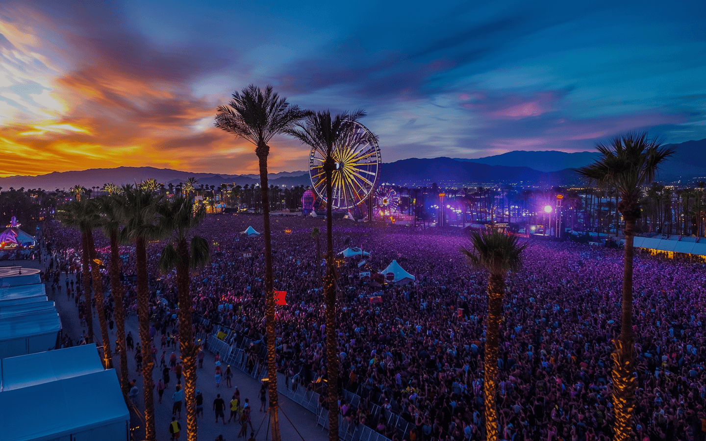 Outdoor festival at dusk: dense crowd, palm trees, a glowing Ferris wheel, and colorful stage lights with distant mountains under a purple sky.