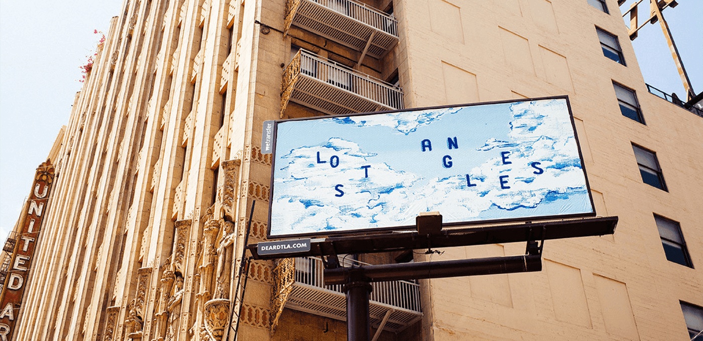 Beige retro building with tall vertical columns and balconies; a large billboard shows blue letters spelling LOS ANGELES against a cloudy sky.