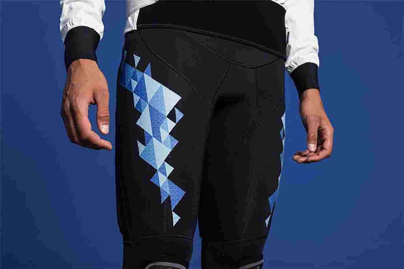 Lower-body view of a person in black athletic pants with a blue triangular pattern on the left leg, and a white long-sleeve shirt, against blue background.