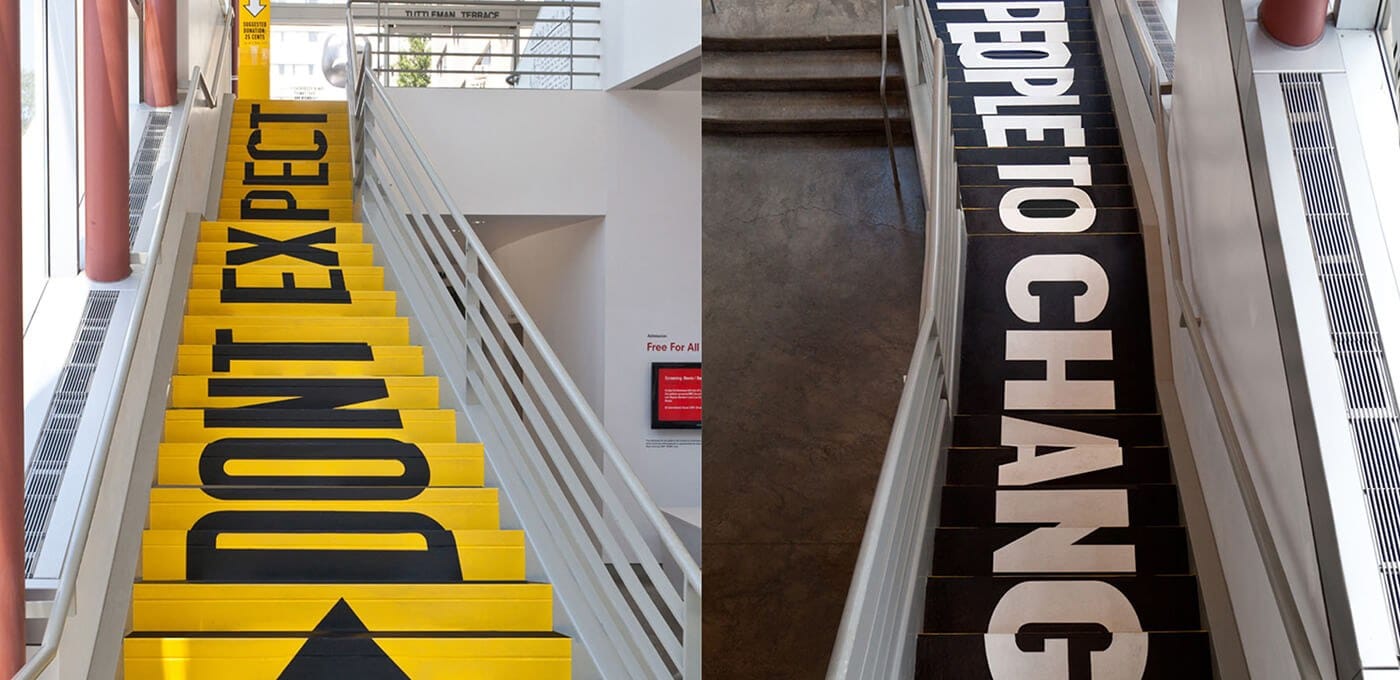 Split view of two staircases in a modern building: left bright yellow steps with large black letters, right dark steps with bold white letters along metal railings.
