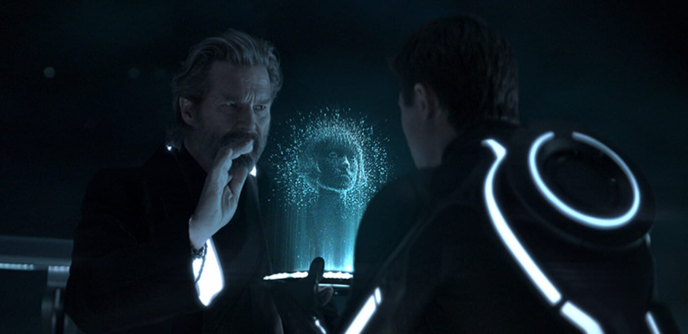 Two figures in a dark, futuristic room face each other; a blue, particle-based hologram of a face glows between them, with luminous rings along their clothing.