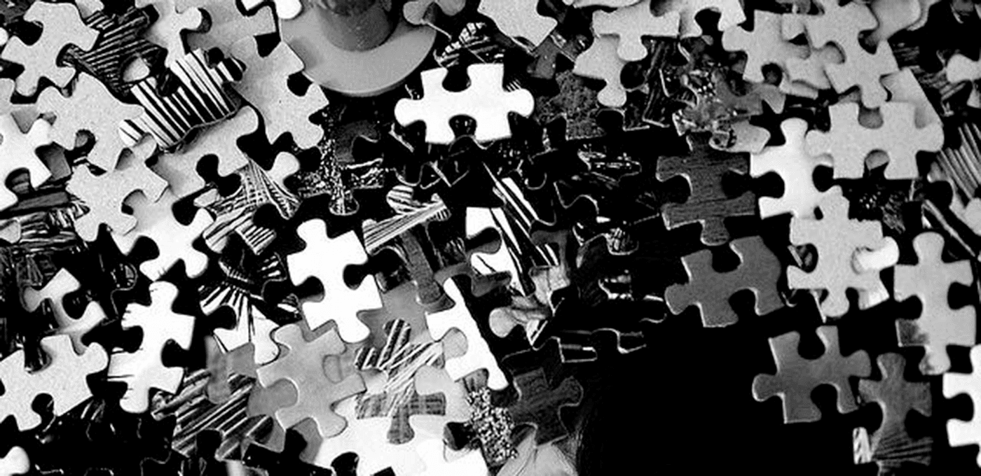 Close-up of many interlocking jigsaw puzzle pieces in grayscale, scattered and overlapping across the frame.
