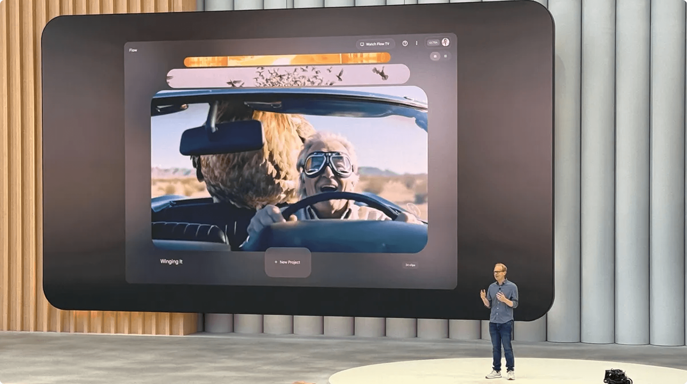 Presenter on a stage beside a curved screen displaying a layered UI with a photo of a driver wearing goggles in a car, and a furry animal in the back seat.