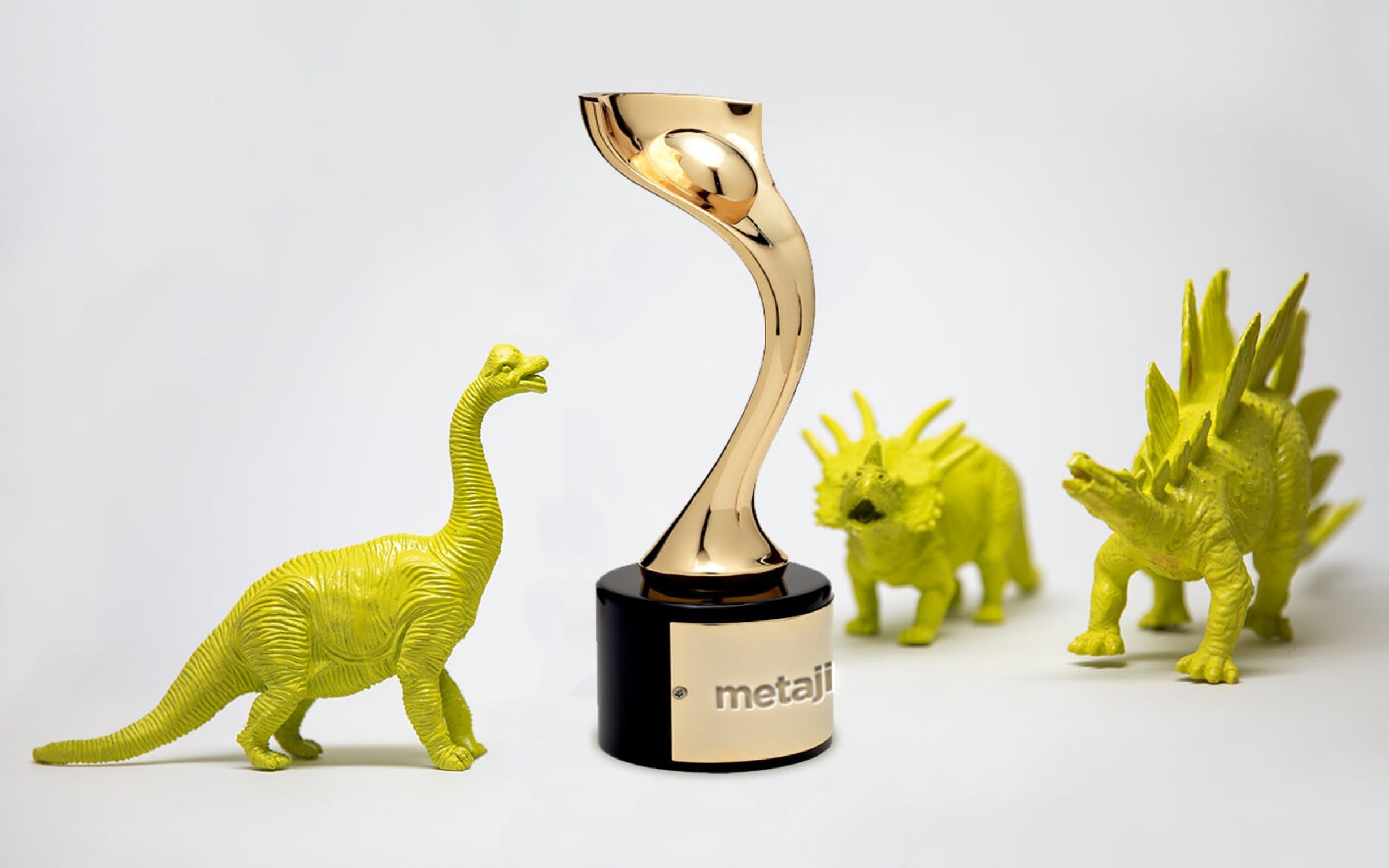 A shiny gold trophy on a black base sits among three neon yellow-green dinosaur figurines on a white background.