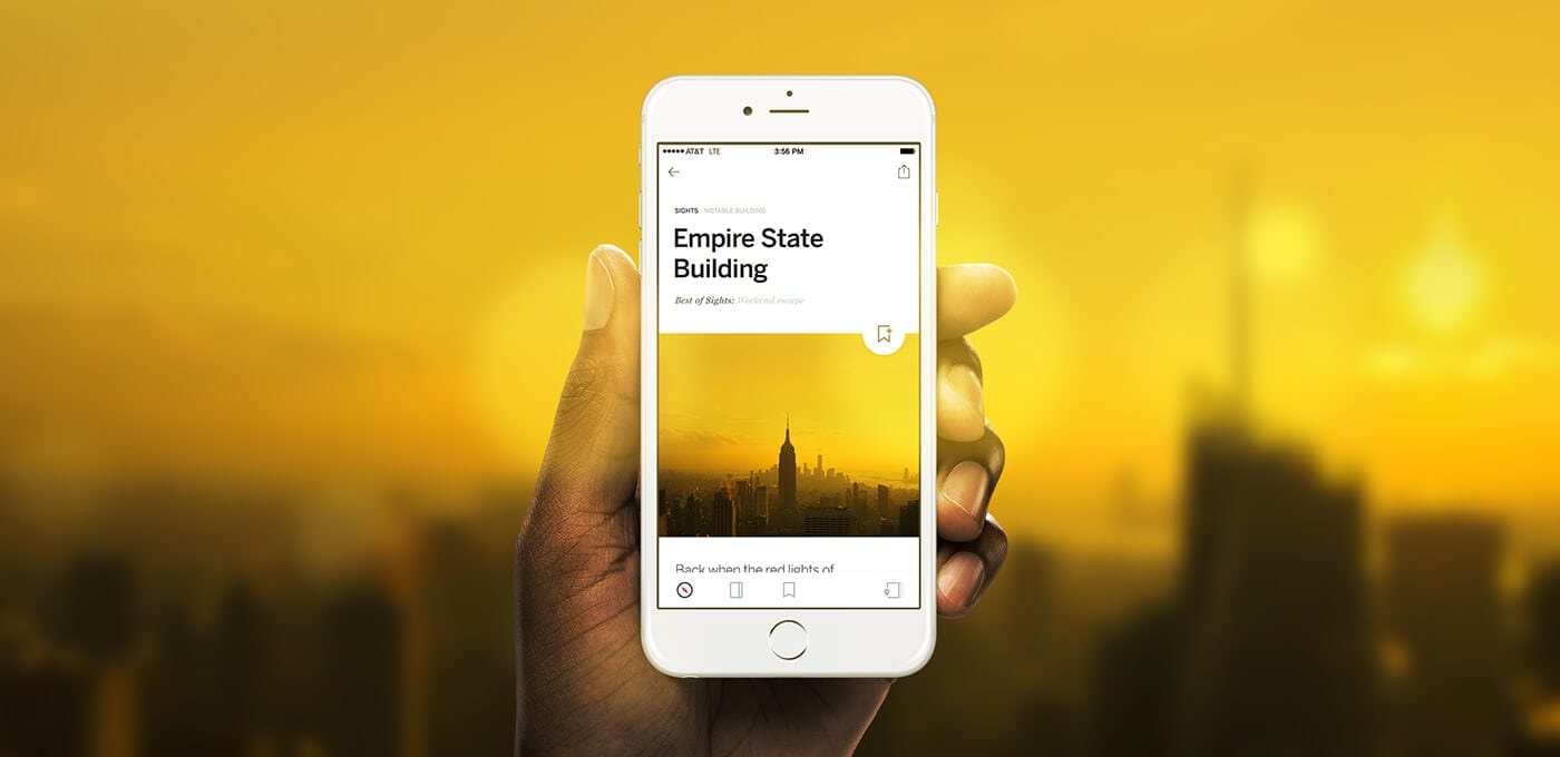 A hand holds a white smartphone displaying a city skyline app titled "Empire State Building" against a blurred yellow sunset backdrop.
