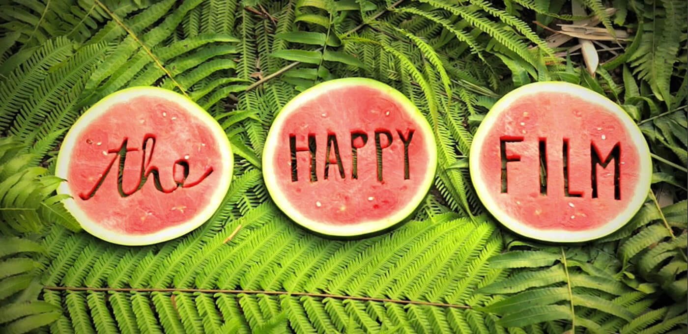 Three watermelon halves on bright green ferns with carved text: middle reads HAPPY and right reads FILM, left side featuring cursive letters.
