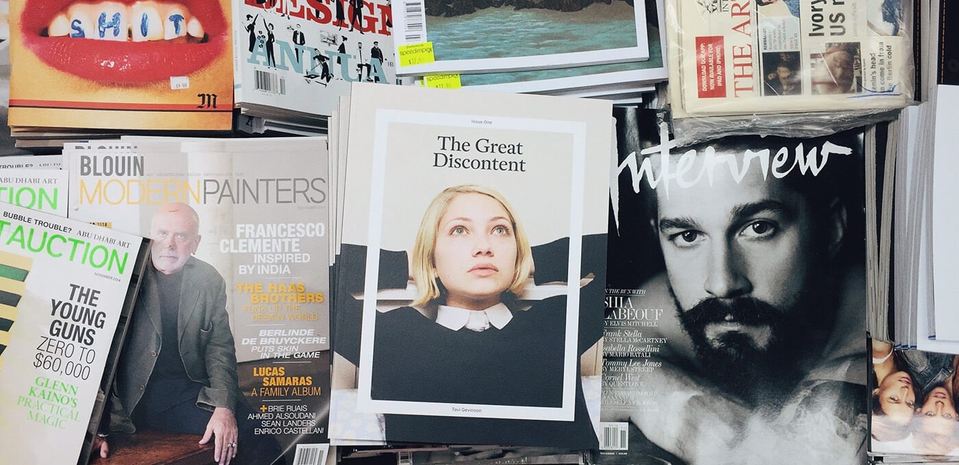 Cluttered magazine rack with various covers; center features The Great Discontent with a blonde person, next to a black-and-white Interview portrait.