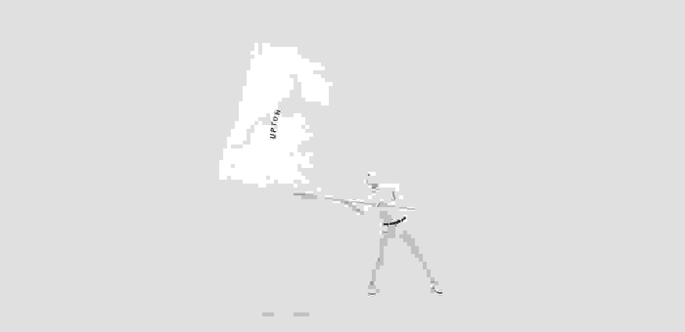 A person windsurfing on a board, gripping a large white triangular sail against a pale gray background.